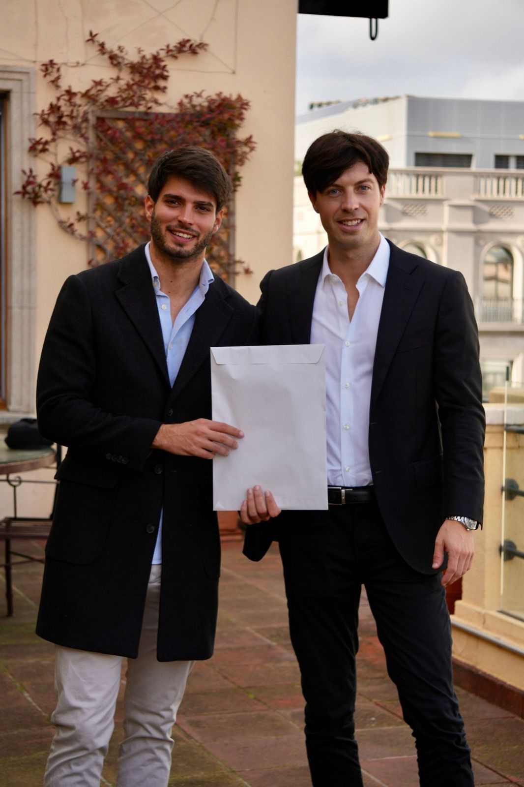 Olaf Groenewegen and his business partner Alberto on a terrace, holding a white envelope between them