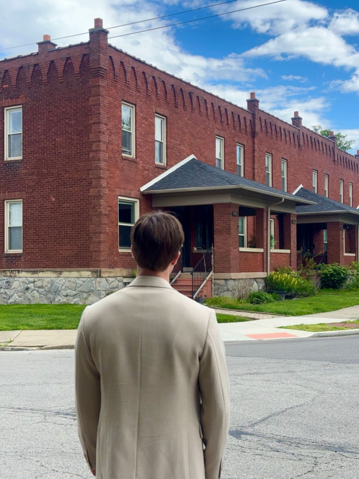 A man in a beige jacket, seen from behind, looking at a red-brick row of houses